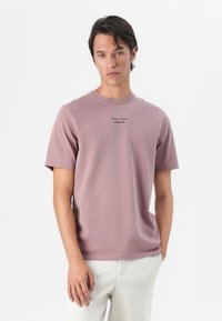 Short-sleeved, crew neck t-shirt in soft, faded mauve cotton. Features a small printed logo in black centered on the chest.