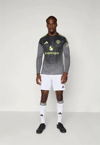 Szürke hosszúujjú mez fekete és sárga részletekkel, grafikával, fehér rövidnadrággal és fekete focicipővel.