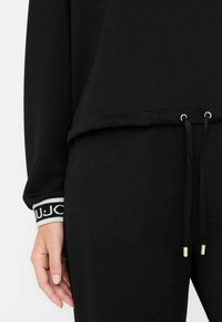 Čierne loungewear s voľným strihom, textúrovanou tkaninou, šnúrkou s zlatými akcentmi a manžetami s logom.