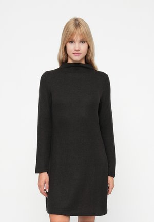 Svart klänning i tröjstil med hög halsringning, långa ärmar och ribbad struktur. Faller ovanför knäna med sidslitsar.