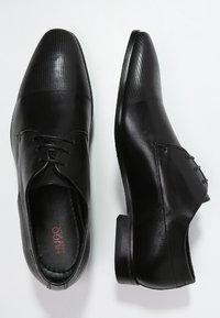 Chaussures habillées en cuir noir au design élégant, avec un orteil texturé et des côtés lisses. Les lacets et l'orteil arrondi complètent le look.