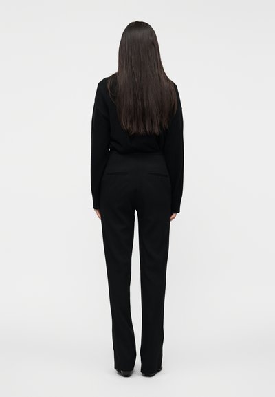 Pull en maille noir et pantalon noir sur mesure, avec une taille haute et une coupe droite. Tissu lisse, design minimaliste, vue de dos.