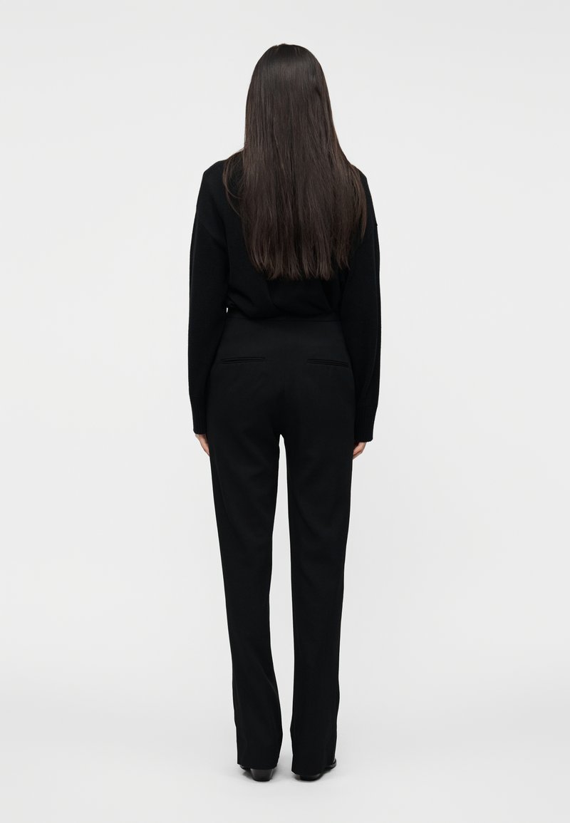 Pull en maille noir et pantalon noir sur mesure, avec une taille haute et une coupe droite. Tissu lisse, design minimaliste, vue de dos.