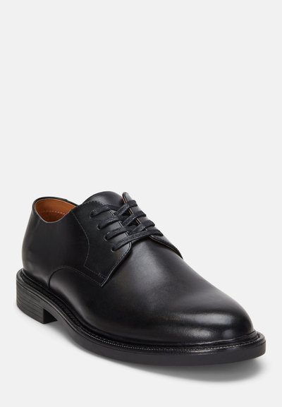 Zapato negro de cuero con cordones, punta redondeada, textura suave y tacón bajo apilado. Costuras sutiles y forro interior color marrón claro.