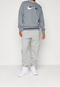 Grå sweatshirt med svart och silver logotyp, i kombination med ljusgrå sweatpants. Vita sneakers fulländar den sportiga stilen.