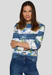 Bluse mit blauen und weißen Streifen, Sternmustern, Dreiviertelärmel und Denim-Textur am Saum, getragen mit dunkelblauen Jeans.