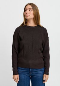 Mörkbrun stickad tröja med ett strukturerat mönster, rund halsringning och ribbad mudd, tillsammans med blå jeans.