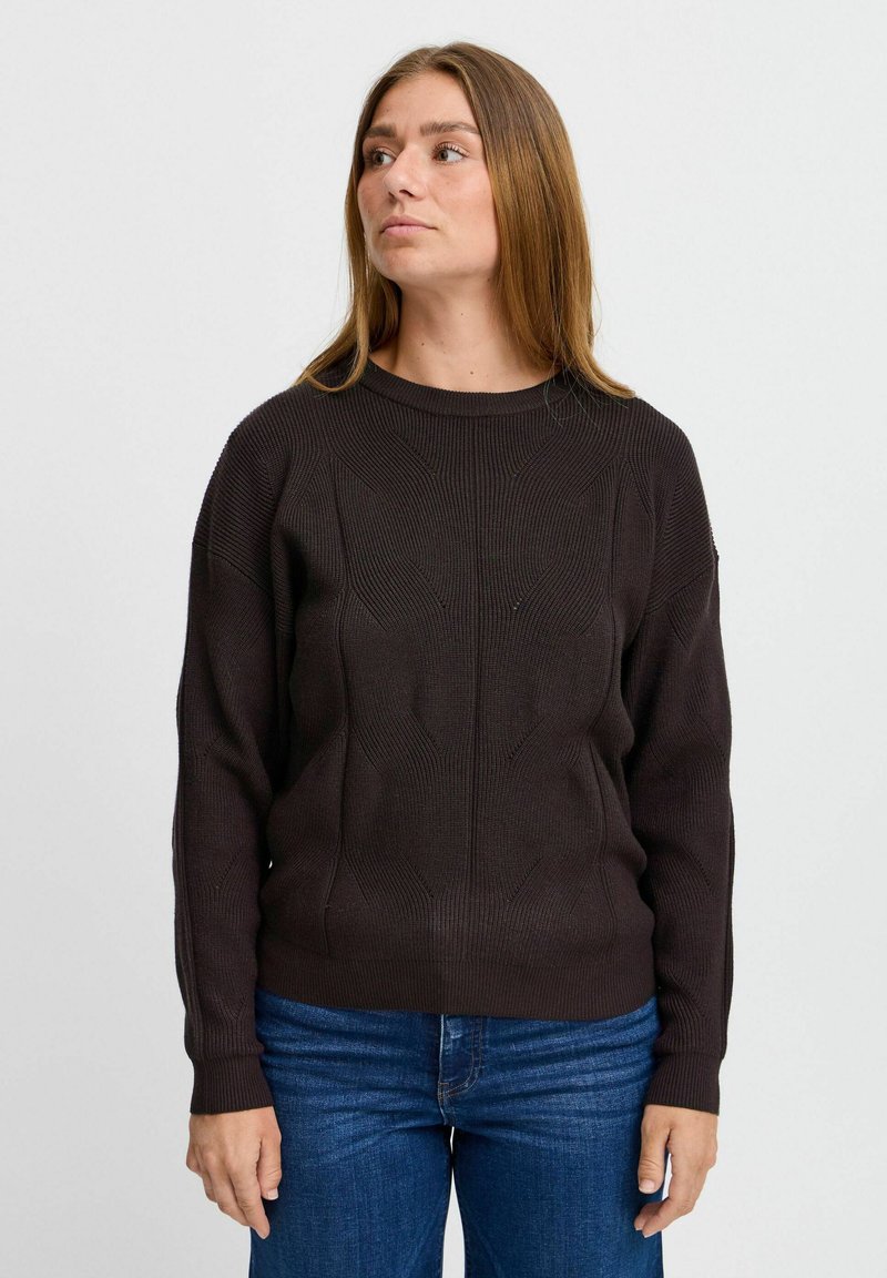 Mörkbrun stickad tröja med ett strukturerat mönster, rund halsringning och ribbad mudd, tillsammans med blå jeans.