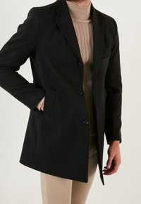 Cappotto in misto lana nero con design su misura, chiusura monopetto con bottoni e tasche laterali. Presenta un colletto a bavero e una texture liscia.