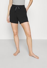 Zwarte shorts van zacht stof, met een relaxed fit, zijzakken en een satijnen lint dat in de taille is geknoopt. Glad textuur.