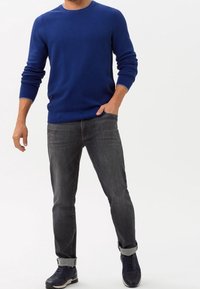 Blå ribbad tröja, grå jeans, uppvikta ärmar, marinblå sneakers. Enkel design, mjuk textur, avslappnad passform, med rundad halsringning.