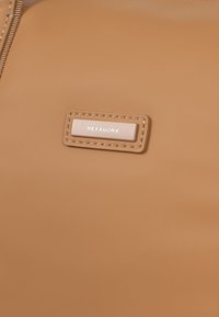 Borsa sintetica color tan con una consistenza liscia, dotata di un tag rettangolare impresso con la scritta "HEXAGONA", circondato da un bordo cucito.