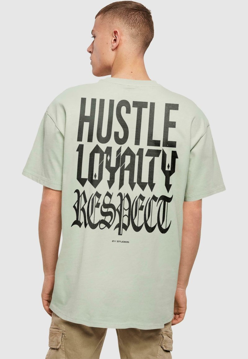 Světle zelené oversized tričko s výraznou černou typografií na zádech: "HUSTLE LOYALTY RESPECT," s jedinečnými, stylizovanými písmeny.