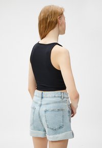 Top corto negro de canalé combinado con pantalones cortos de mezclilla azul claro, con dobladillo deshilachado y bolsillos traseros. Vista desde atrás.