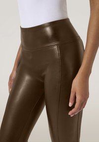 Leggings in ecopelle marrone con vita alta, caratterizzati da una texture liscia e una vestibilità slanciata. I dettagli delle cuciture migliorano il design.