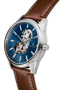 Kraftig stålklokke med blå skive, eksponert mekanisk urverk, sølvfargede detaljer, og et brun lærrem med tekstur.