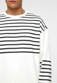 Wit langemouwen shirt met opvallende zwarte horizontale strepen. Heeft een klassieke ronde hals en een zachte, gestructureerde stof.