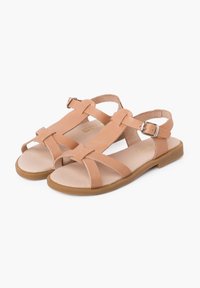 Sandali in pelle tan con suola piatta, caratterizzati da cinturini incrociati e una fibbia alla caviglia. Texture liscia con dettagli di design minimalisti.