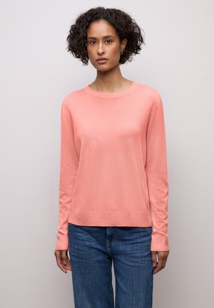 Jasnoróżowy sweter z długim rękawem o miękkiej fakturze, z okrągłym dekoltem i ściągaczami na mankietach, w połączeniu z niebieskimi szerokimi jeansami.