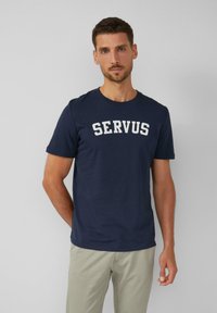 Granatowa bawełniana koszulka z krótkim rękawem, z białym, pogrubionym napisem "SERVUS" na piersi. Okrągły dekolt.