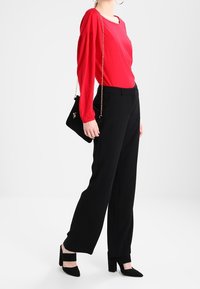 Rode longsleeve top met een ronde hals, gecombineerd met zwarte hoog waist wijde broek. Geaccessoireerd met een zwarte schoudertas en hakken.