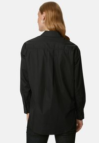 Camicia nera in cotone con spalla posteriore, colletto ripiegato, maniche lunghe e polsini con bottoni. Presenta un taglio dritto e una texture liscia.