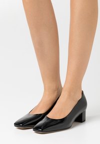 Černé lakované kožené lodičky se čtveratou špičkou a nízkým blokovým podpatkem. Hladký povrch, minimalistický design a žádné viditelné ozdoby.