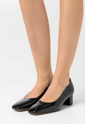 Zapatos de tacón de charol negro con punta cuadrada y tacón bajo. Textura suave, diseño minimalista y sin adornos visibles.