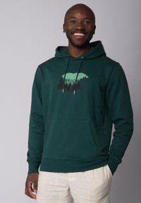 Grüne Kapuzenjacke aus einem Baumwollgemisch mit einer Bären-Silhouette, die Walddetails in kontrastierenden hellgrünen und dunklen Schattierungen zeigt.