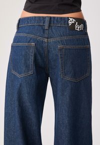 Wijde denimbroeken in donkerblauw, met een hoge taille, zichtbare stiksels en een zwart label met witte letters op de achterband.