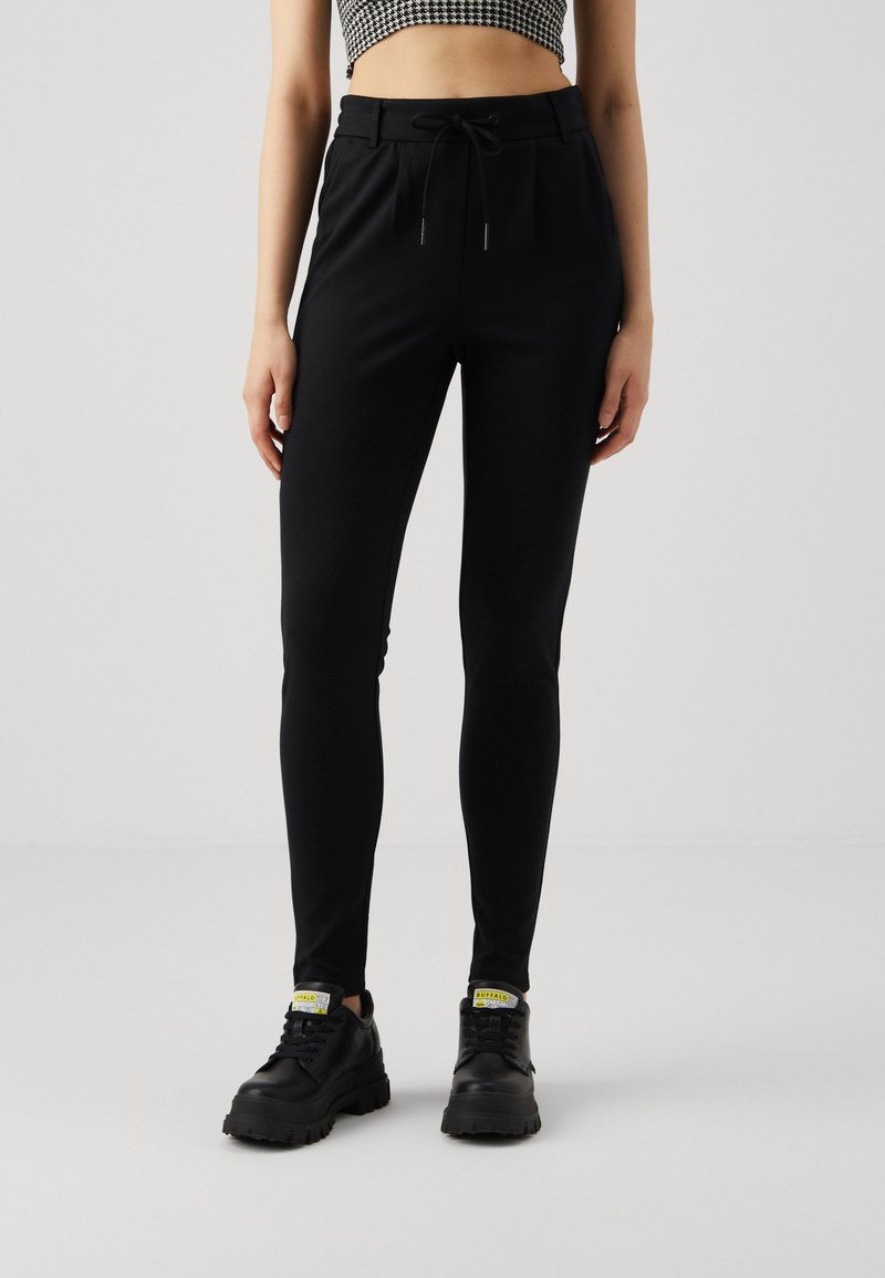 Sorte, tettsittende joggebukser med elastisk midje og snøring; kombinert med store sorte sneakers med gule detaljer.