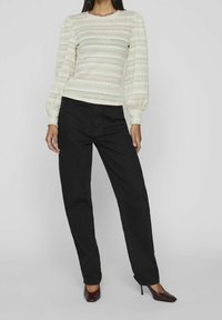 Top en tricot crème avec un motif texturé et des manches bouffantes, associé à un pantalon noir taille haute et des escarpins à bout pointu.