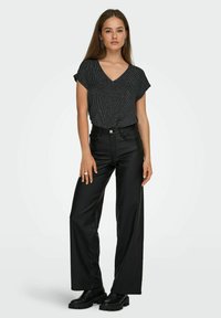 Sort tekstureret V-hals top med korte ærmer, kombineret med højttaljede bukser i bredt ben i imiteret læder og chunky sorte støvler.