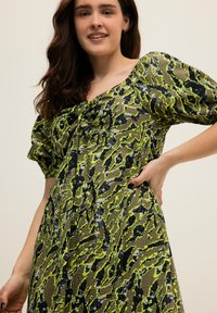 Grün und schwarz gemustertes Kleid mit Rundhalsausschnitt, Puffärmeln und Raffung am Dekolleté. Glattes Gewebe mit leicht strukturiertem Finish.