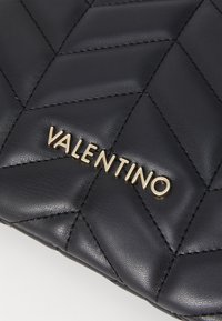 Černá prošívaná kožená taška s zlatým logem "VALENTINO". Povrch je hladký s výraznými diamantovými vzory a viditelným prošitím.