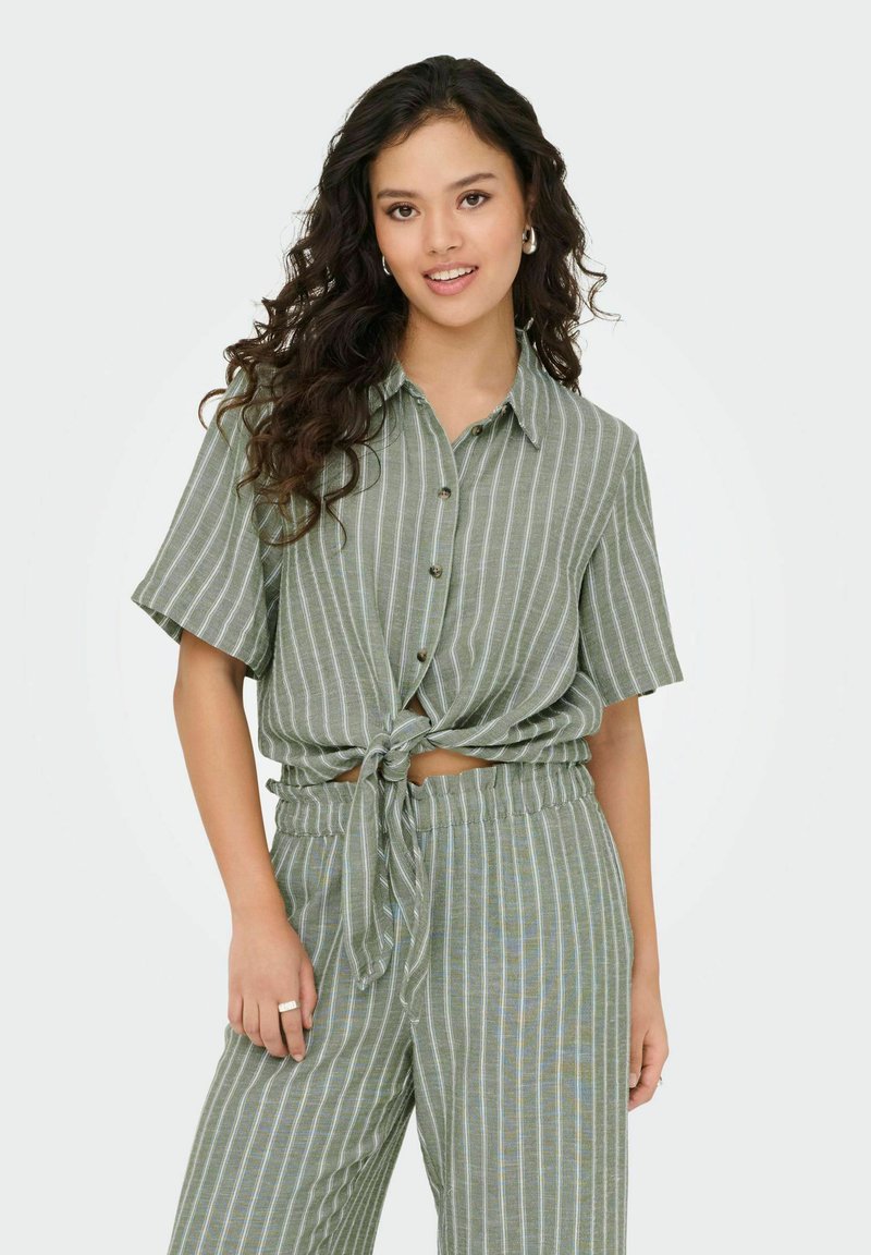 Groen gestreepte shirt met korte mouwen en een geknoopt voorpand, gecombineerd met bijpassende wijde broek. De stof lijkt lichtgewicht en gestructureerd.