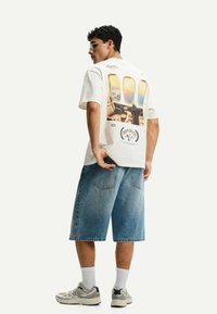 Witte graphic t-shirt met een kleurrijke print van een vliegtuigraampje op de achterkant. In combinatie met losse, lichtblauwe denim korte broek.