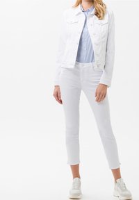 Veste en denim blanche avec deux poches poitrine, associée à une chemise rayée bleue et blanche et à un jean skinny blanc, complétée par des baskets blanches.