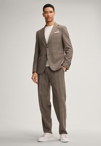 Brązowy garnitur w kratę o dopasowanym kroju, składający się z marynarki z jednym guzikiem, pasujących spodni i białych sneakersów. Lekki materiał, gładka tekstura.