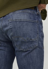 Jeans in denim blu scuro con un design classico, tasche posteriori con dettagli di cucitura e una texture leggermente sbiadita.