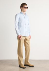 Light blue button-up shirt, cream trousers, and brown ankle boots. The shirt has a smooth texture, with long sleeves and a classic collar.