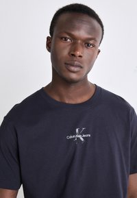 Navy blue cotton t-shirt featuring a white Calvin Klein Jeans logo and a graphic “K” on the chest. Short sleeves, round neck design.