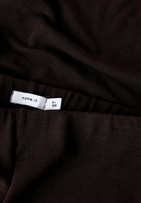 Smeđi rebrasti materijal s glatkom teksturom. Uključuje bijelu etiketu s natpisom "name it", veličina "8Y" i upute za njegu.