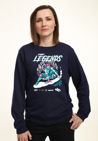 Námořnická mikina se světlou barevnou grafikou skateboardisty s růžovými vlasy. Obsahuje text "STREET LEGENDS" a detaily loga.