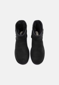 Botas de tobillo de ante negro con un forro interior suave y peludo. Presentan una punta redondeada y un detalle de costura en contraste a lo largo de la suela.