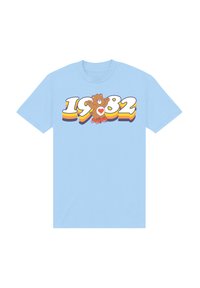 Světle modré bavlněné tričko s karikaturou medvídka se srdcem, rokem "1982" a barevným vrstevnatým textovým designem.