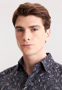 Camicia con motivo scuro caratterizzata da un design paisley in tonalità di blu, bianco e marrone. Collo corto e vestibilità aderente, con tessuto liscio al tatto.