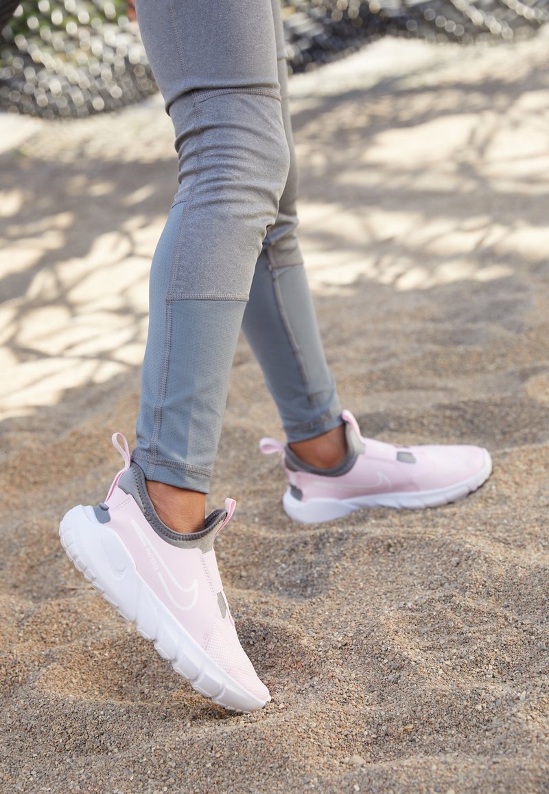 Baskets de sport roses avec des accents gris, conçues dans un style à enfiler et dotées d'une semelle rembourrée, associées à des leggings gris ajustés.