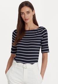 Haut à rayures bleu marine et blanches à manches courtes avec un col bateau, fabriqué à partir d'un tissu lisse, associé à un pantalon crème et une boucle de ceinture circulaire.