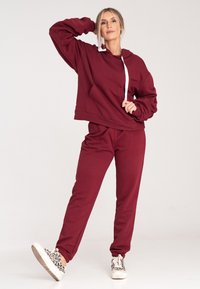 Burgundowa bluza z kapturem z białym sznurkiem, kieszenie z przodu; w połączeniu z dopasowanymi dresami, miękka tekstura, elastyczne mankiety i dół.